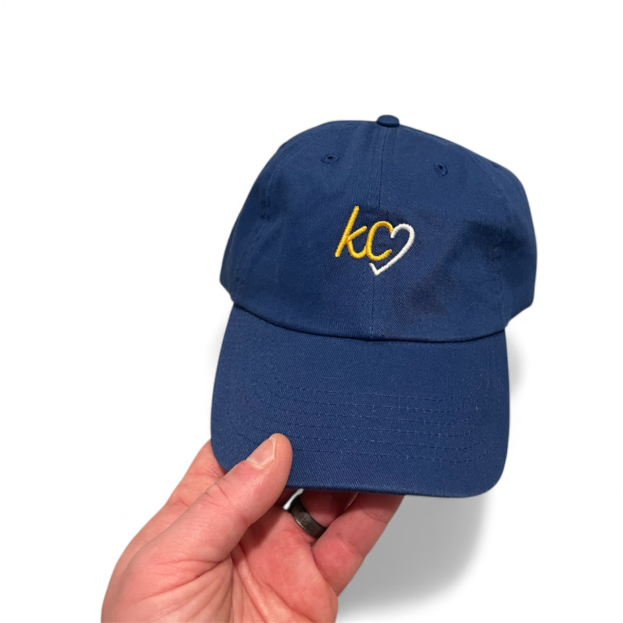 Blue cap with 'kc' logo held by a hand on a white background